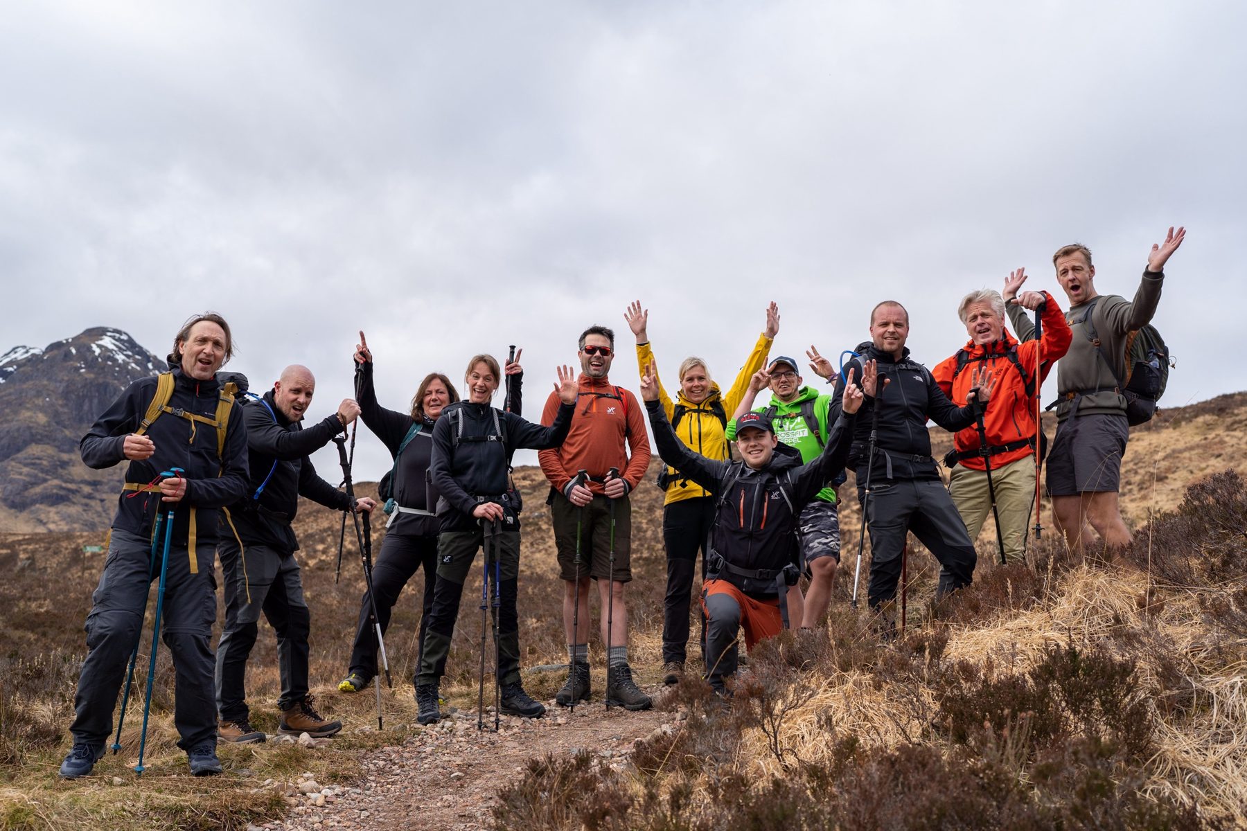 Een juichende groep wandelaars van De Tocht op de West Highland Way, met besneeuwde bergen van Glencoe op de achtergrond